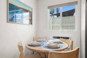 A dining table set with plates, glasses, and cutlery, a painting on the wall, and a window with a view of a building and palm trees. - Pacific Tides -Entire 9-Unit Apartment Complex w/ Parking + A/C in Pacific Beach (San Diego)