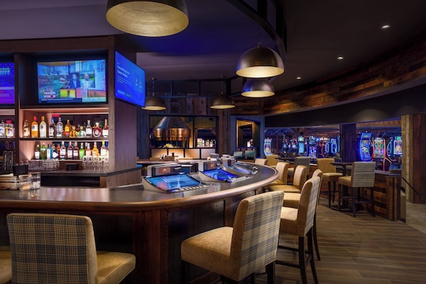 Un espace bar avec un comptoir, des tabourets de bar et des jeux d’arcade.