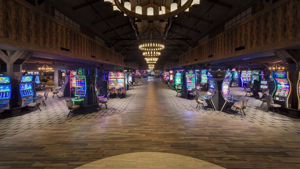 A spacious casino interior with multiple gaming machines, a central chandelier, and a wooden floor.