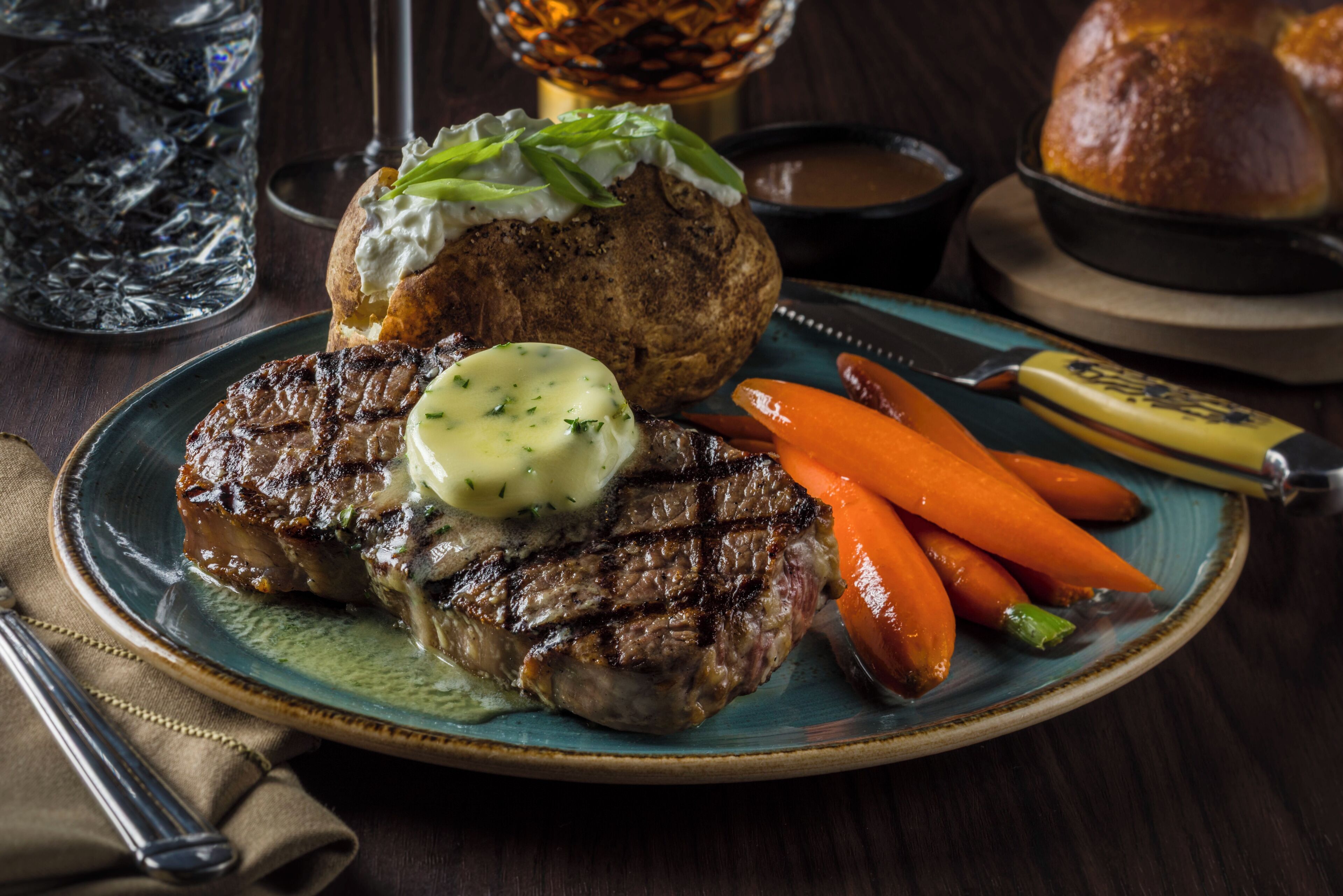 Un plato con un filete a la parrilla, una patata al horno y zanahorias.