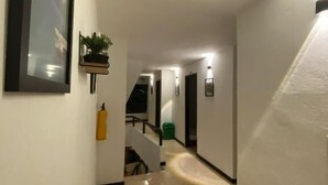 A hallway with a marble floor, a framed picture on the left, a small plant on a shelf, and a staircase at the end. - Hotel Galería Plaza (Santa Bárbara)