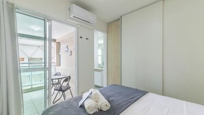 Une chambre d’hôtel comprenant un lit, une petite table avec des chaises, un balcon avec une porte vitrée et un appareil de climatisation.