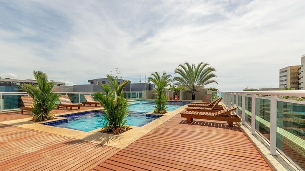 Un espace piscine aménagé sur le toit, avec une terrasse en bois, des chaises longues et des plantes tropicales.