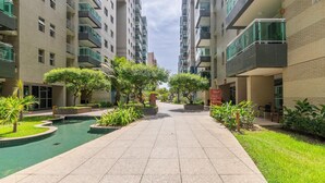 Un immeuble résidentiel moderne doté de nombreux balcons, d’une cour intérieure agrémentée d’un élément aquatique et entouré de verdure.
