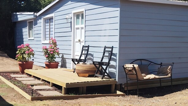 A small, single-story building with a wooden deck, two potted plants, and a bench. - Cozy cottage in Sto Domingo, quiet environment, close to beach and commerce. (San Antonio)