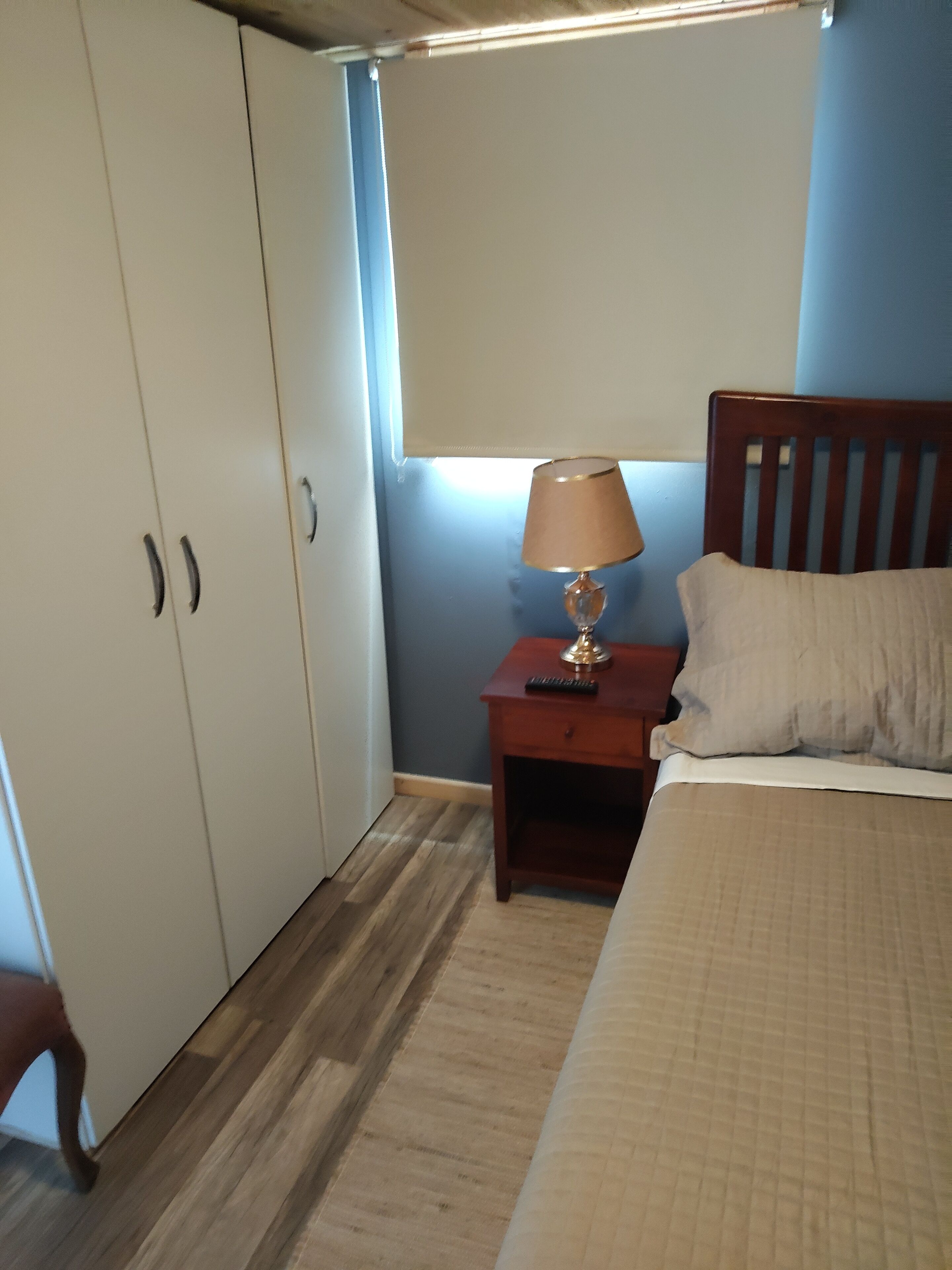 A bedroom with a bed, a nightstand with a lamp, a wooden headboard, and a wardrobe.