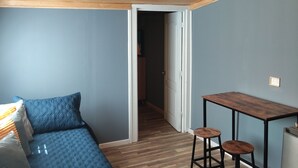 A room with a wooden ceiling, a bed with blue bedding, a small table with two stools, and a door leading to another room. - Cozy cottage in Sto Domingo, quiet environment, close to beach and commerce. (San Antonio)