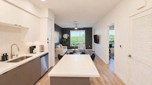 Een moderne keuken met een centraal eiland, een zithoek met een bank en uitzicht op groen.