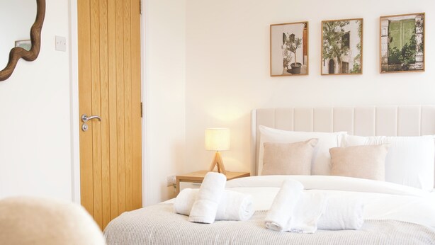 A neatly made bed with white linens and pillows, a wooden door, and three framed pictures on the wall.