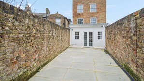 A narrow alleyway with a white building at the end, flanked by brick walls.