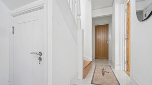 A hallway with a white door, a wooden door at the end, and a doormat with "welcome" written on it.