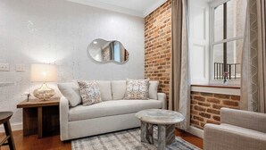 A modern living room with a sofa, a round coffee table, a side table with a lamp, a mirror, and a brick accent wall.