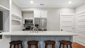 A modern kitchen with white cabinetry, a large island with stools, stainless steel appliances, and a recessed ceiling light.