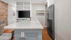 A modern kitchen with a marble countertop, built-in shelving, a large refrigerator, and a flat-screen TV.