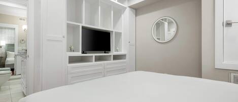 A bedroom with a large bed, built-in TV, storage cabinets, and a round mirror on the wall.