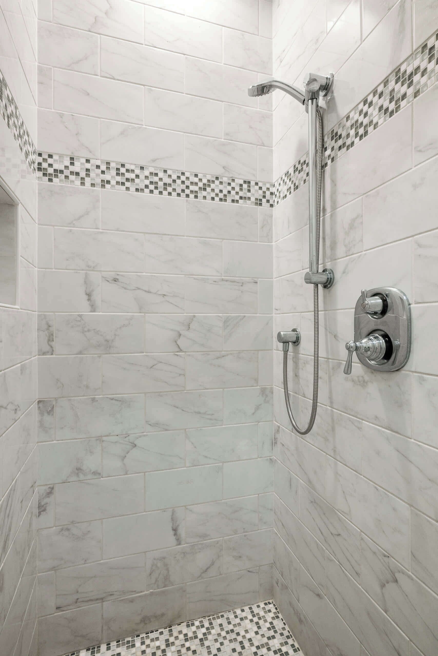 Eine Dusche mit Handbrause und Bedienfeld an der Wand.
