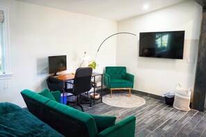 A modern living room with a desk, two green armchairs, a TV, and a large window. - San Jose Studio • Near PayPal Park • EV & BBQ (San Jose)