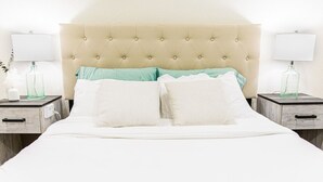 A bed with a tufted headboard, two bedside tables with lamps, and a nightstand with a bottle.
