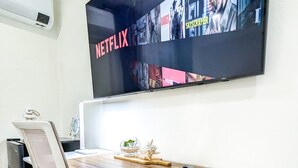 A modern office space with a white desk, ergonomic office chair, and a mounted TV displaying Netflix content.