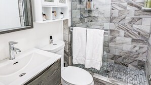 A modern bathroom with a glass shower enclosure, white fixtures, and marble-patterned tiles.