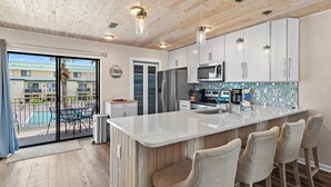A modern kitchen with a large island, bar stools, and a view of a pool. - Sandprints A8 (Destin)