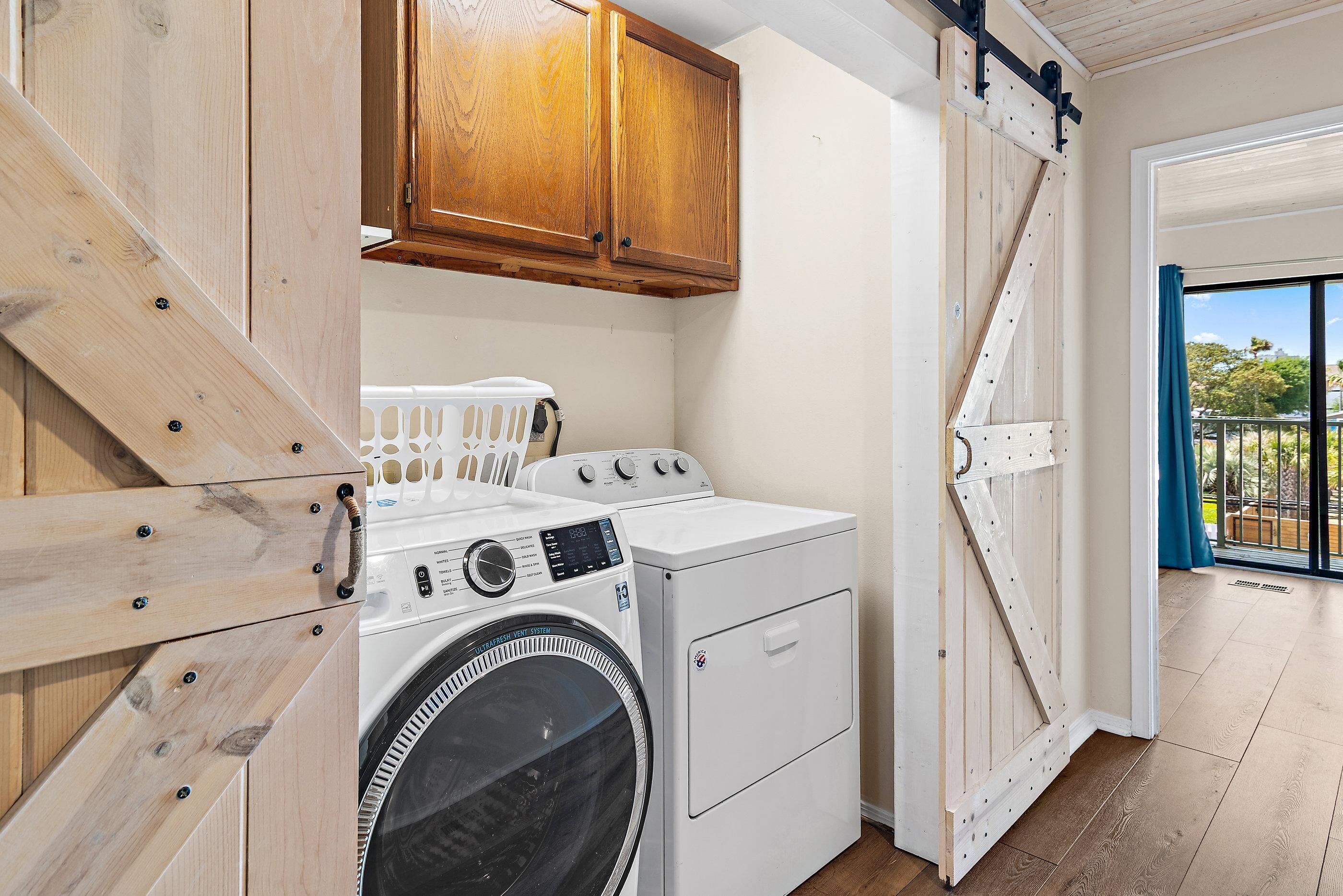 A laundry area with a washing machine, dryer, wooden cabinets, and a sliding door leading to an outdoor balcony.