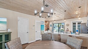 A kitchen with a round dining table, wicker chairs, a chandelier, and a view of the beach through the window. - Sandprints A8 (Destin)