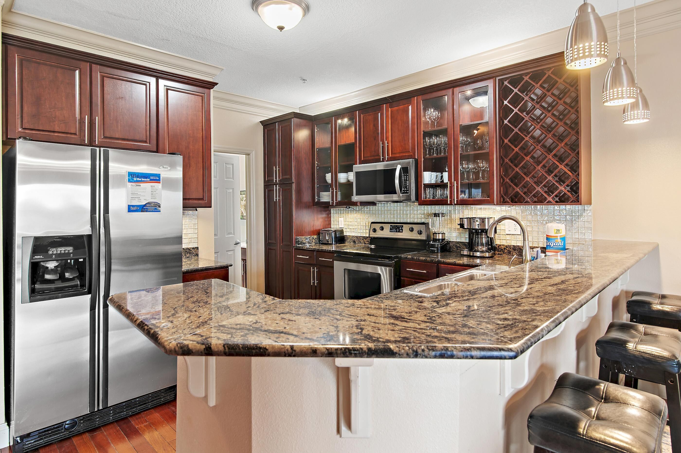 A kitchen with dark wooden cabinets, stainless steel appliances, a granite countertop, and a wine rack.
