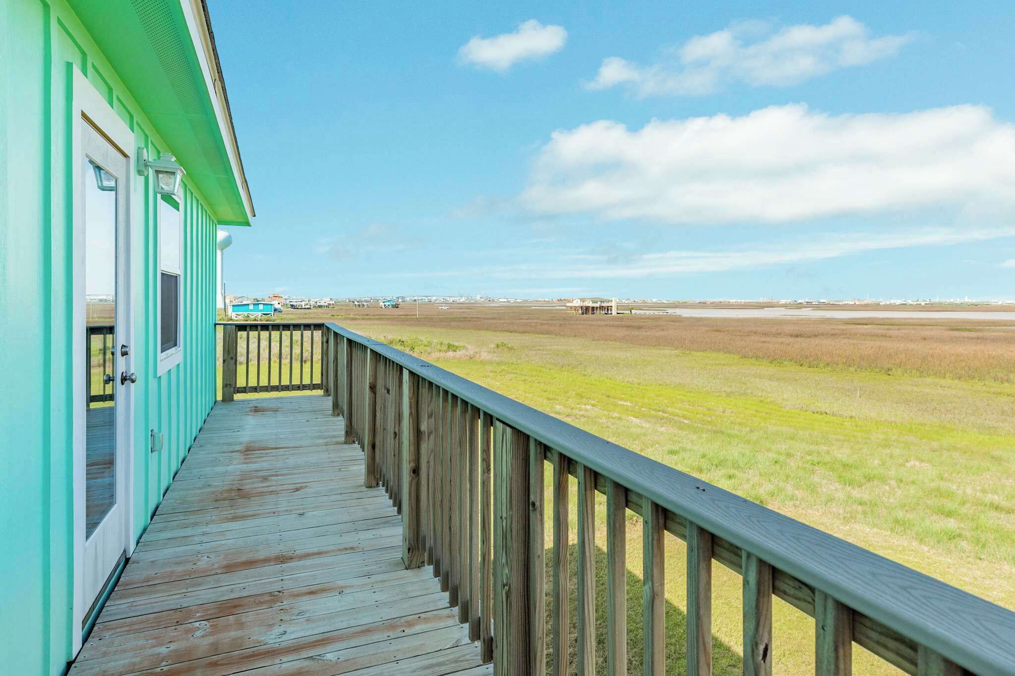 Une terrasse en bois mène à un bâtiment aux couleurs turquoises, qui offre une vue sur un paysage plat.