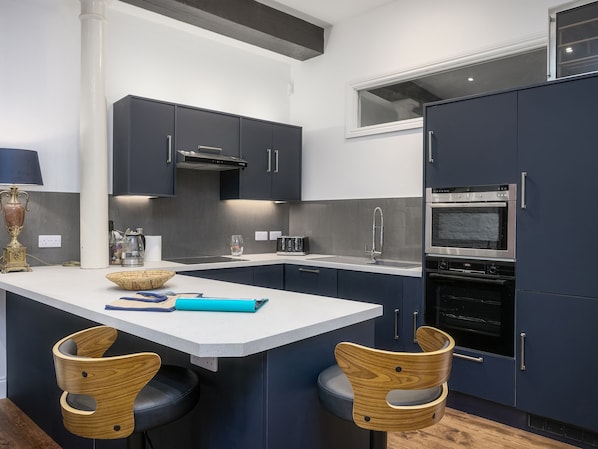 A modern kitchen with dark cabinets, a white countertop, a built-in oven, and two wicker chairs.