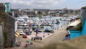 A marina with boats docked, a paved area with tables and chairs, and buildings in the background. - The Mayflower Suite (Plymouth)
