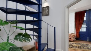 A blue spiral staircase with a wooden floor, a framed picture on the wall, and a red curtain on a door. - The Mayflower Suite (Plymouth)