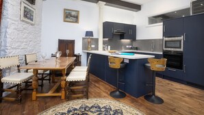 A kitchen with a central island, dark cabinets, and a dining area with wooden chairs and a table. - The Mayflower Suite (Plymouth)
