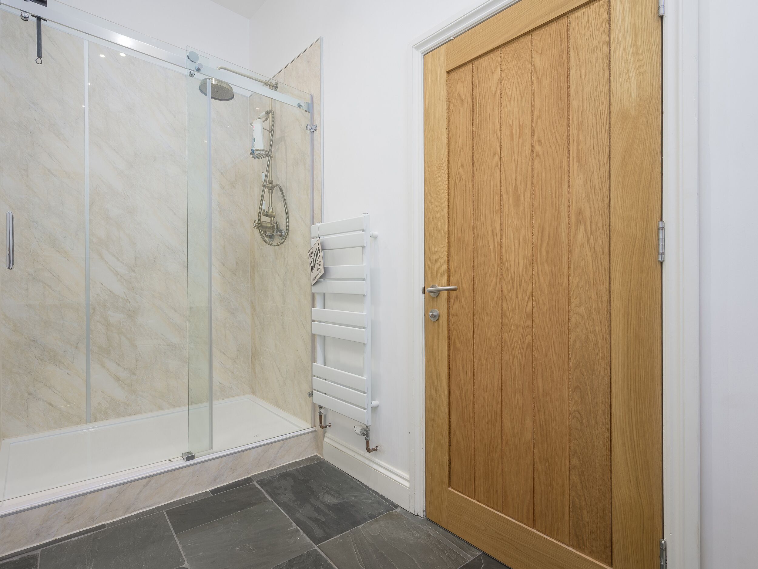 A bathroom with a glass shower enclosure, a wooden door, and a white towel rack.