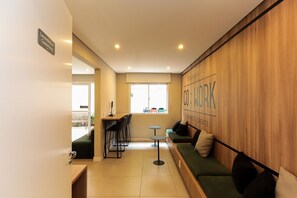 A modern coworking space with a wooden accent wall, a green sofa, and a small table. - Apto c Academia Perto do Allianz na Barra Funda (São Paulo)