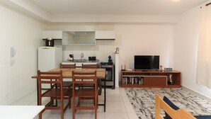 Una cocina moderna con armarios blancos, una mesa de comedor con sillas, una estufa empotrada y un televisor de pantalla plana sobre un soporte de madera.