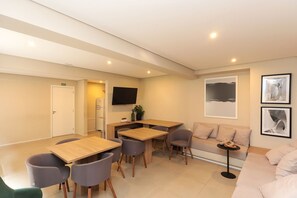 A modern living room with a sofa, a dining table with chairs, a flat-screen TV mounted on the wall, and framed artwork on the wall. - Apto c Academia Perto do Allianz na Barra Funda (São Paulo)