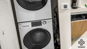 Ein kleiner Waschbereich mit zwei übereinander gestapelten Waschmaschinen, einer Flasche von Tide Waschmittel und einer Kaffeemaschine auf einer Arbeitsplatte.