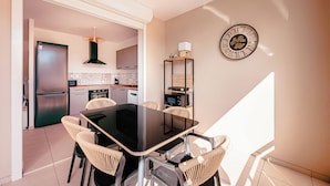 Una cocina moderna con comedor, que incluye una mesa negra, sillas de mimbre y un reloj de pared decorativo.