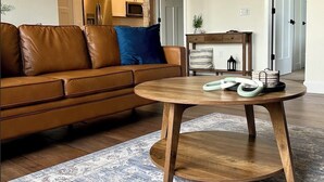 Un salon avec un canapé en cuir marron, une table basse ronde en bois et un tapis à motifs.
