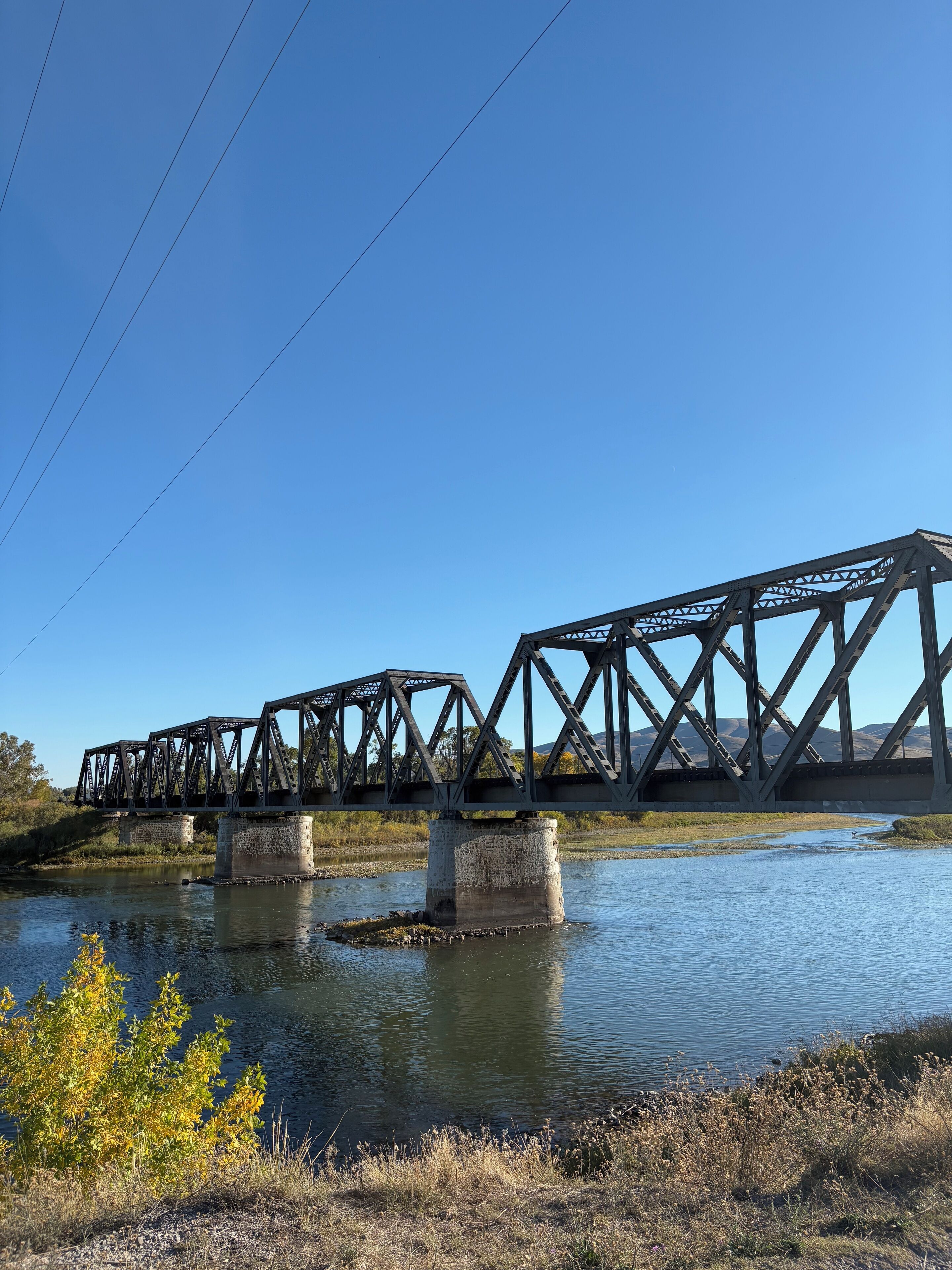 A steel bridge over a calm river with clear skies.