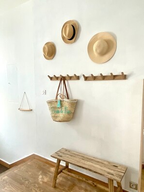 Ein Zimmer mit einer hölzernen Bank, einem an der Wand befestigten HutfĂ€nger mit HĂŒten, einem gewebten Korb mit Schrift und einer kleinen, dreieckigen Dekoration.