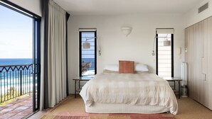 Een slaapkamer met een groot bed, uitzicht op de oceaan en een balkon met een hekwerk.
