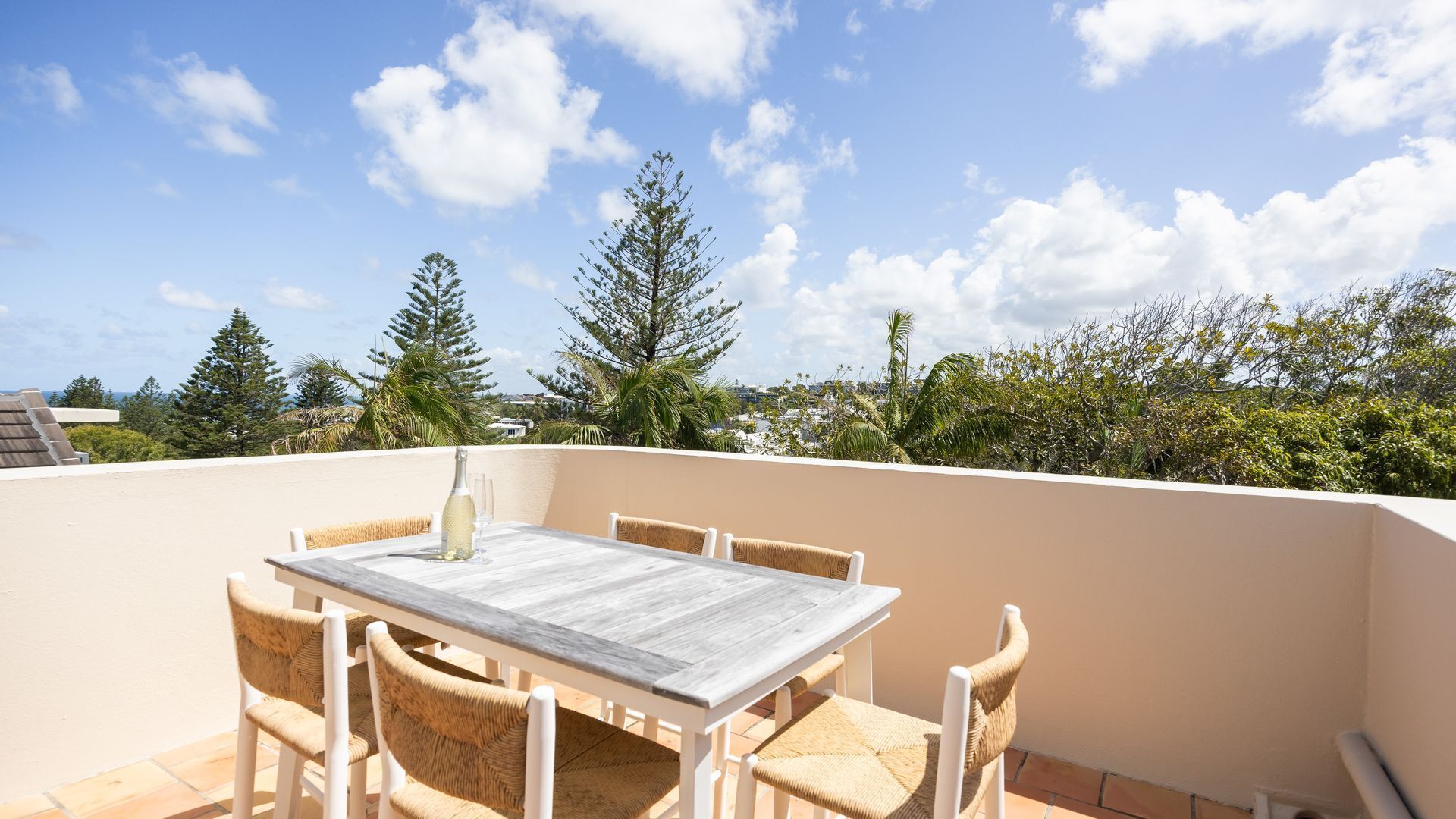 A terrace with a table and chairs, overlooking a landscape with trees and a clear sky.