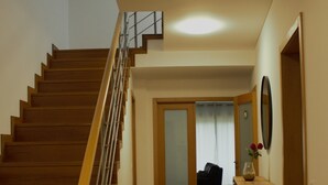 Una escalera de madera que conduce a un segundo piso, un pasillo con un armario y un jarrón, y una puerta con un espejo.