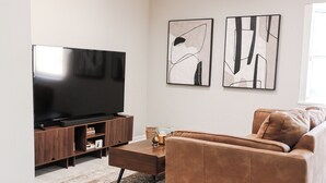 Una sala de estar moderna con un televisor de pantalla plana sobre un mueble de madera, un sofá de cuero marrón, una mesa de centro y arte abstracto en la pared.