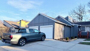 En boligs garage med et 'Må ikke parkeres' skilt, en grå pickup lastbil parkeret i indkørslen, og et hus med grå facade og en hvid garageport.
