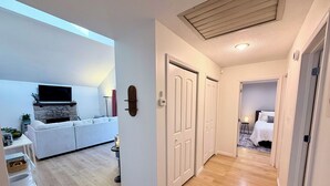 En moderne stue med sofa, TV, pejs og en gang der fører til et soveværelse.