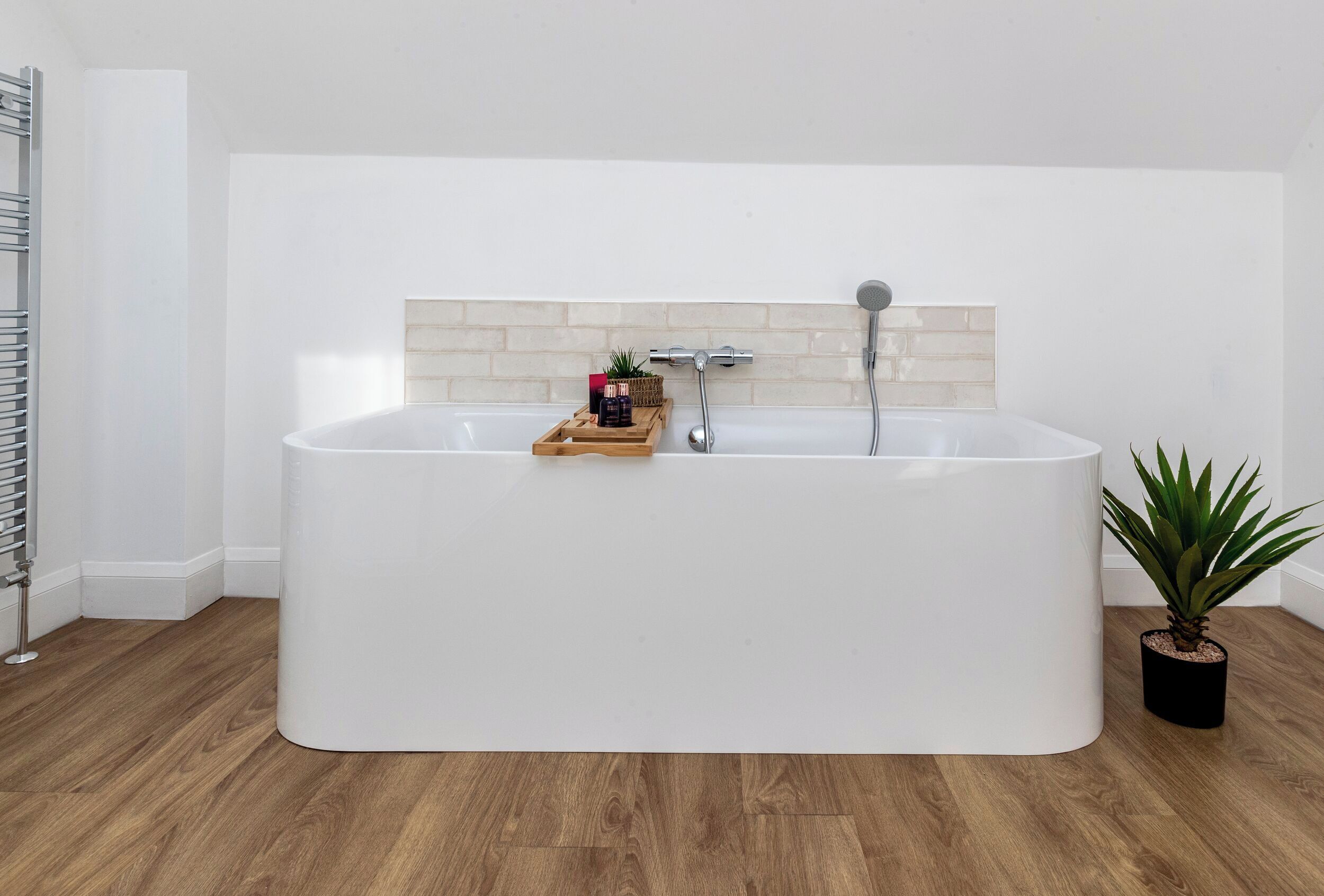 Een moderne badkamer met een vrijstaand bad, een handdoekhouder, een potplant en een houten dienblad met toiletartikelen.