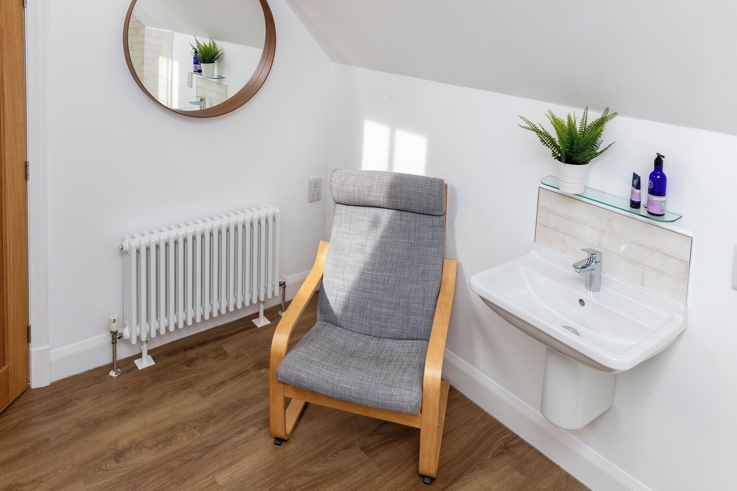 A room with a chair, a radiator, a sink, a mirror, and a potted plant.